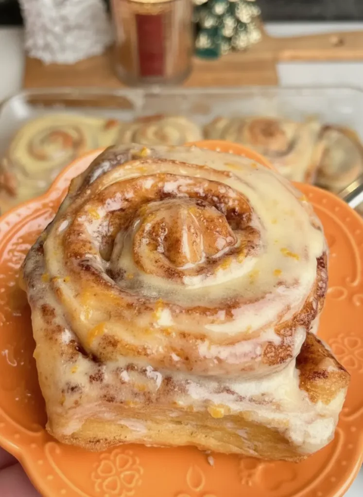 Orange Cinnamon Rolls An ingredient focus shot on a marble countertop. A small wooden bowl is filled with bright orange zest next to a pile of white flour and a stick of softened butter. A wooden spoon rests nearby. Soft shadows, clean presentation, morning light. 3:4 aspect ratio.
