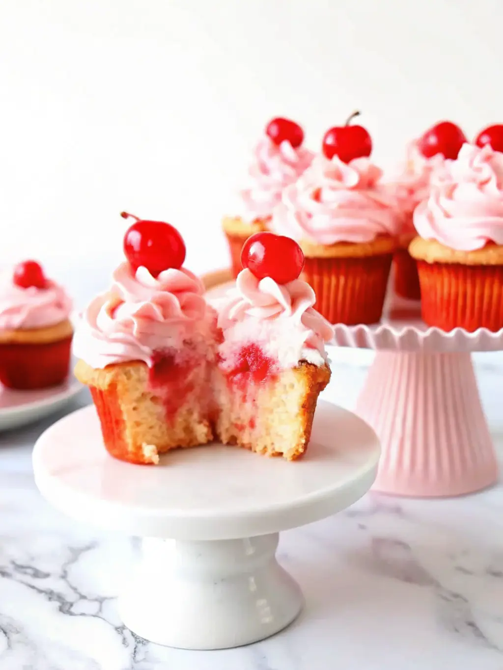 A wire rack holding freshly baked, unfrosted pink Cherry Chip Cupcakes cooling on a marble countertop. A simple, clean white ceramic bowl of homemade pink cherry buttercream frosting is visible nearby. Natural morning light with soft shadows. NO HANDS OR PEOPLE. (3:4 ratio)