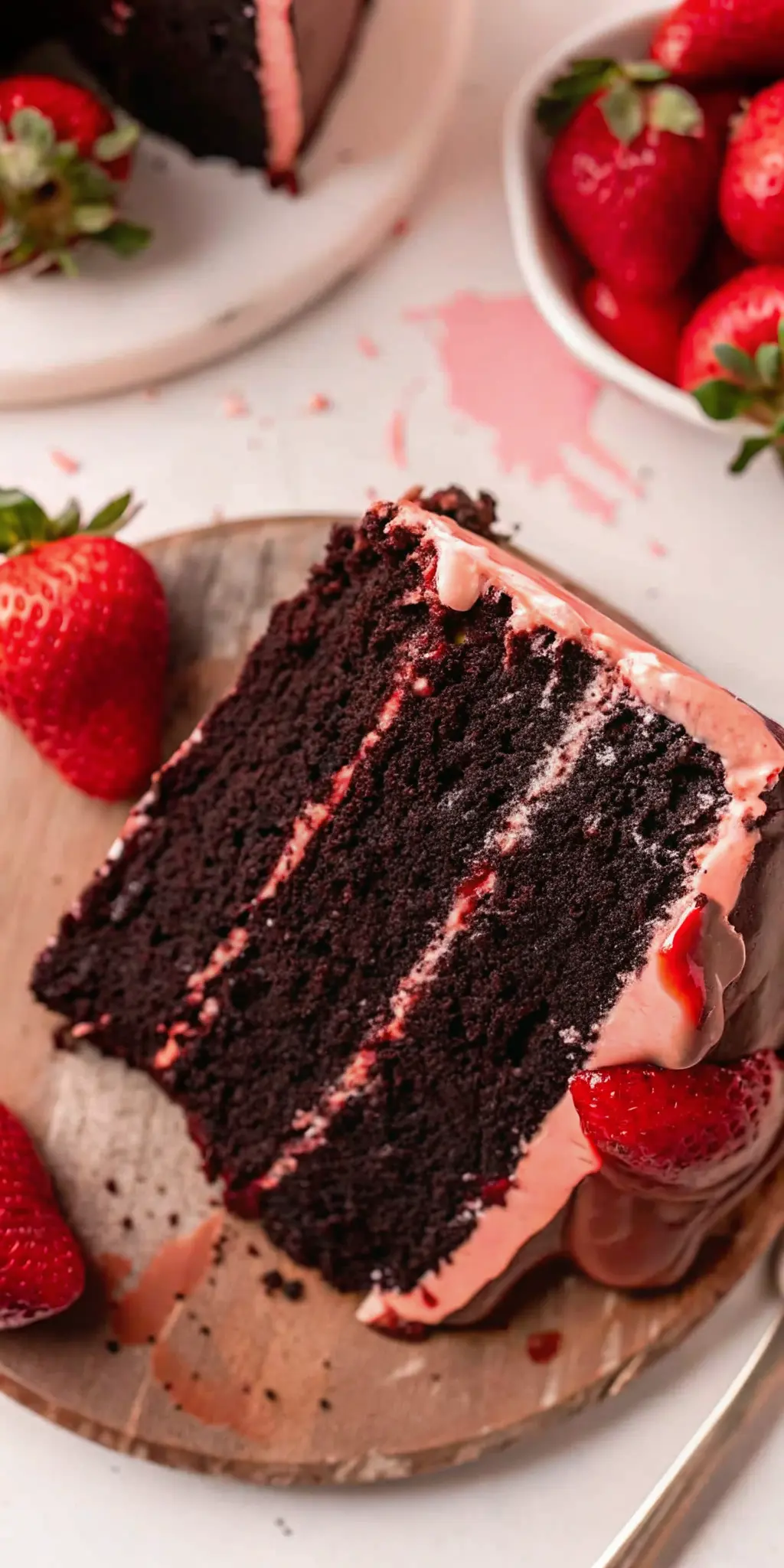 A detailed close-up of a slice of Chocolate Covered Strawberry Cake, emphasizing the moist texture of the dark chocolate cake layers, the creamy consistency of the pink strawberry buttercream, and the glistening chocolate ganache drip. Fresh strawberry halves are visible on the top and next to the cake slice on a white plate. Shot on a marble countertop with natural light, soft shadows, and warm tones. (3:4 ratio).