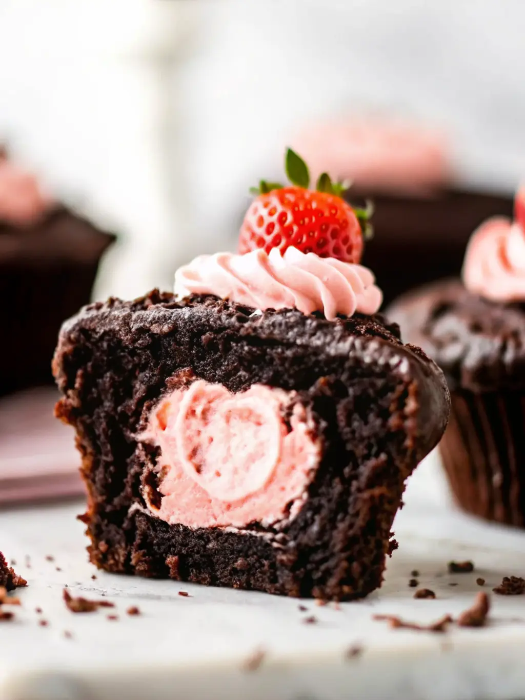 A freshly baked chocolate cupcake on a minimalist white ceramic bowl on a marble countertop, being cored (without hands visible) to show the cavity for the strawberry filling. A small piping bag with pink strawberry cream cheese frosting is ready to fill the cupcake. Natural morning light, warm tones. (3:4 ratio)