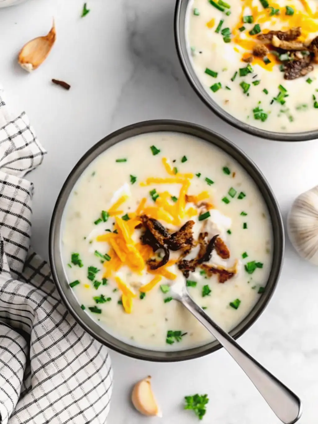 A flat lay (3:4 ratio) showcasing the fresh ingredients for Creamy Vegan Loaded Baked Potato Soup: russet potatoes, a yellow onion, garlic cloves, fresh chives, a small bowl of nutritional yeast, and a carton of plant milk, all artfully arranged on a clean wooden cutting board on a white marble countertop. Natural morning light creates gentle shadows. No hands visible.