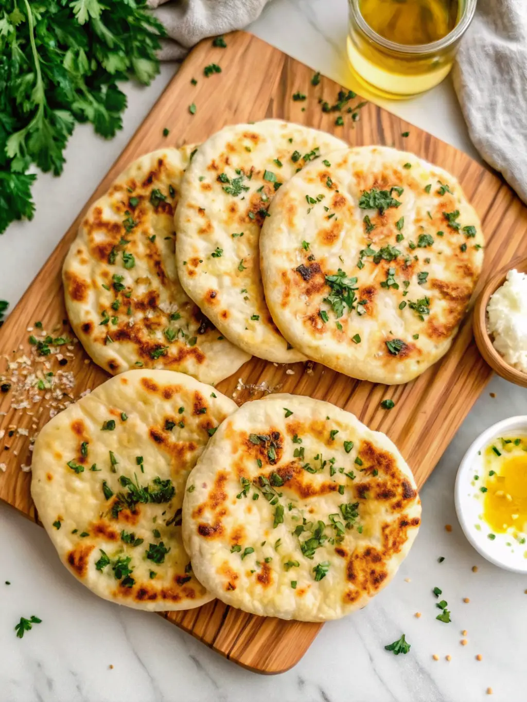 A close-up, angled shot of a torn section of a golden-brown, fluffy cottage cheese flatbread, revealing its airy, tender interior texture. The flatbread is on the signature wooden cutting board, with fresh herbs and a drizzle of olive oil on top. White marble countertop in the background. Soft shadows, warm tones, clean presentation. (3:4 ratio).