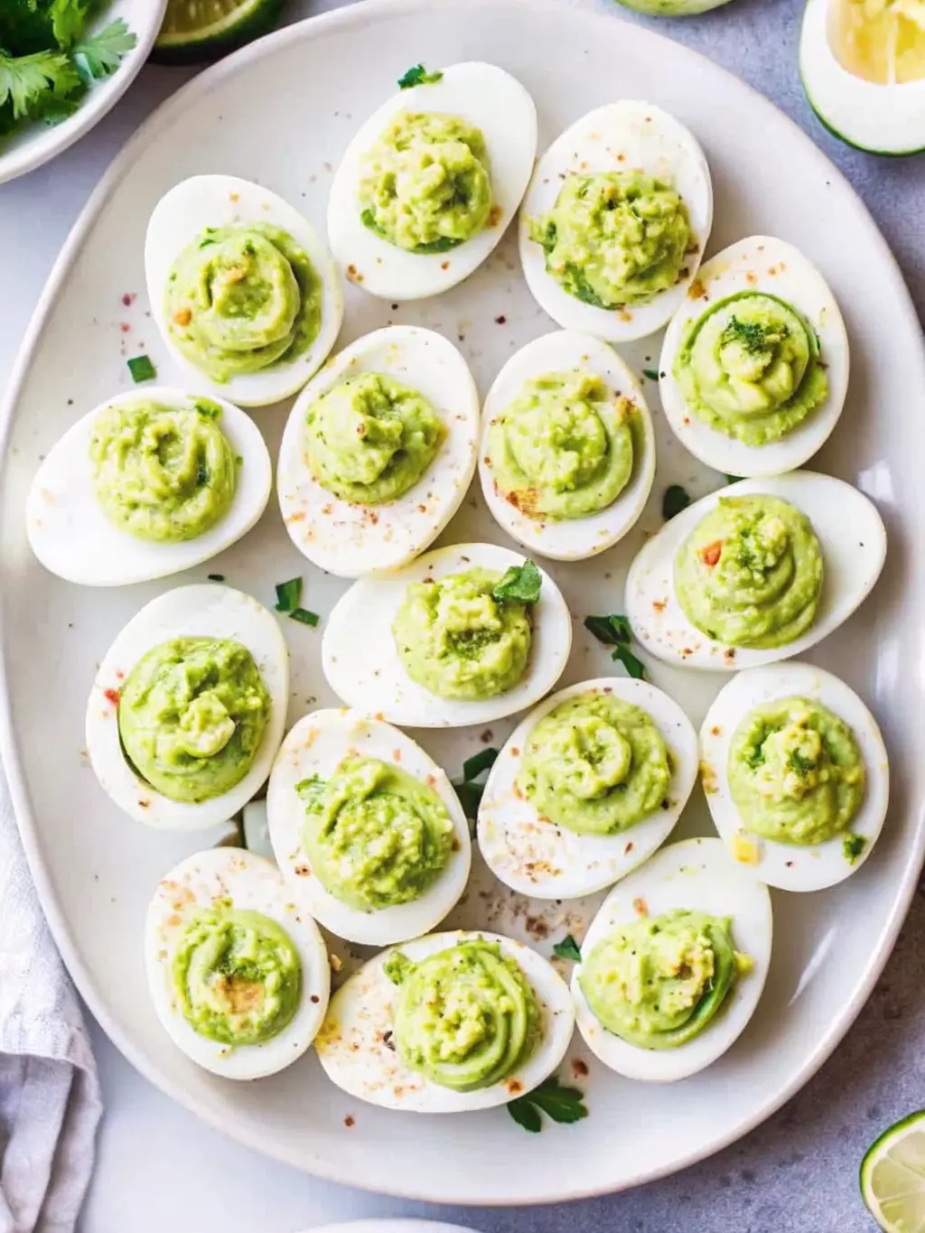 A 3:4 ratio image focusing on the texture and presentation of a few Million Dollar Deviled Eggs on a minimalist white plate. The close-up showcases the creamy, tall, swirled piped yolk filling, the vibrant red of the smoked paprika, and the bright green of the finely chopped chives. The texture of the egg white is smooth and firm. The background is softly blurred, showing hints of the marble countertop and natural morning light. NO HANDS OR PEOPLE.