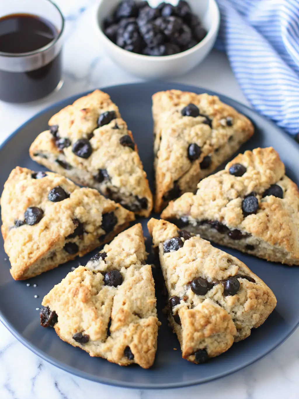 A flat lay of ingredients for Sourdough Chocolate Chip Scones on a light blue/grey marble countertop: a white ceramic bowl of all-purpose flour, a glass measuring cup of sourdough discard, a stick of grated cold butter, a small bowl of dark chocolate chunks, and a sprig of fresh herbs for brand identity, near a wooden cutting board. Natural morning light, soft shadows, warm tones. (3:4 ratio)