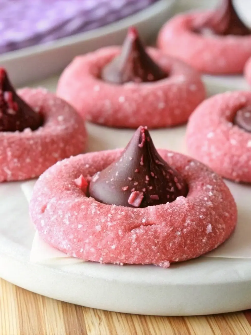 Ingredients for Strawberry Kiss Cookies laid out neatly on a marble countertop. Vibrant pink strawberry flavored gelatin mix, flour, softened butter, granulated sugar, vanilla extract, and a bowl of unwrapped Hershey's Kisses. A wooden cutting board is subtly visible in the background, bathed in natural morning light from an east window. Soft shadows, warm tones, clean and tidy. 3:4 ratio. NO HANDS OR PEOPLE.