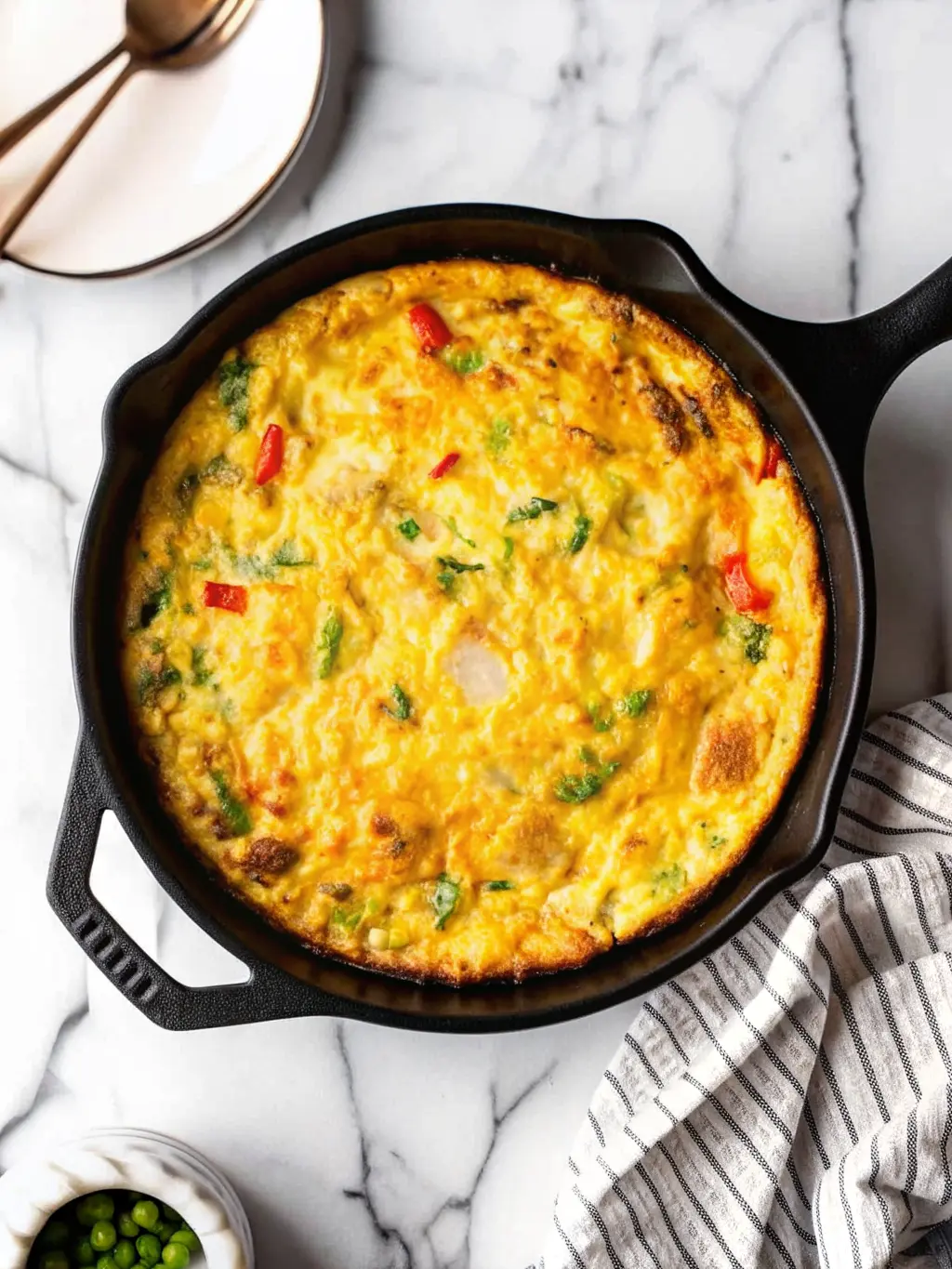 The frittata mixture, golden and studded with colorful vegetables (broccoli, red and green bell peppers), simmering gently in a black cast iron skillet on a stovetop, just before being transferred to the oven. Subtle steam may be rising. The scene is bathed in natural morning light from an east window, with the white marble countertop visible. A ceramic salt and pepper shaker set (one dark, one light, with cork stoppers) is in the soft background. No hands or people. (3:4 ratio)