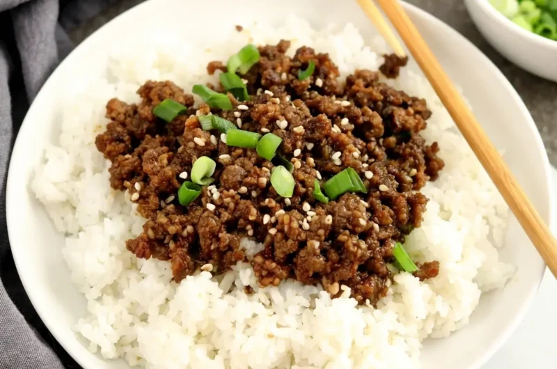 A vibrant Korean Ground Beef Bowl, presented in a minimalist white ceramic bowl on a light marble countertop. The bowl is filled with fluffy white rice, topped generously with savory, dark brown ground beef, scattered with bright green sliced green onions and white sesame seeds. Wooden chopsticks rest on the rim of the bowl. Soft natural morning light from an east window illuminates the scene, creating warm tones and gentle shadows, with a grey linen napkin and a small bowl of fresh green onions blurred in the background, all clean and tidy. (4:3 aspect ratio)