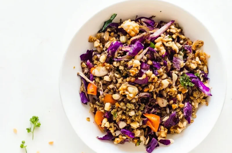 An overhead hero shot of a vibrant Shaved Brussels Sprouts Salad in a minimalist white ceramic bowl on a clean marble countertop, featuring thinly sliced purple cabbage, bright orange diced carrots, light brown grains or nuts, corn kernels, and fresh green parsley garnish. The scene is bathed in natural morning light from an east window, casting soft shadows, with a warm, tidy presentation and a subtle wood accent in the background. No hands or people. (4:3 ratio)