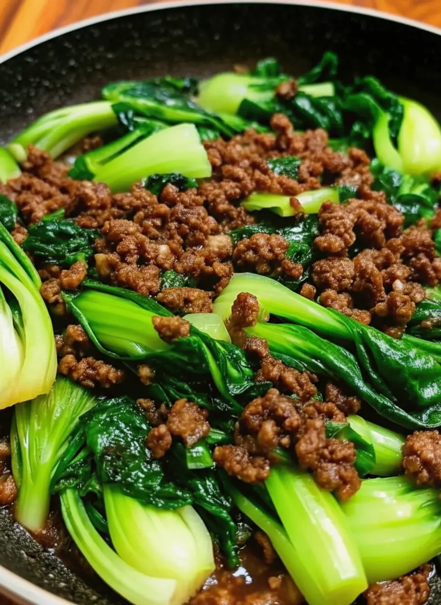 Eye-level shot of ingredients on a well-worn wooden cutting board. Raw baby bok choy halved lengthwise, a mound of raw ground beef, fresh garlic cloves, and a small bowl of dark sauce. The background shows the marble countertop and a hint of white ceramic ware. Soft, natural lighting.