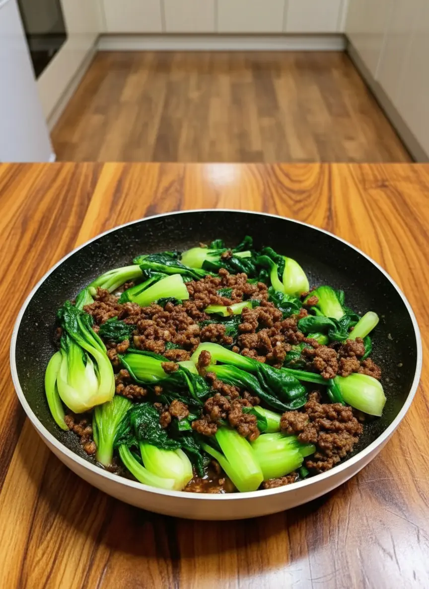 A close-up action shot of the cooking process in the skillet. The ground beef is browned and crispy, and the bok choy is just being added to the pan. The sauce is bubbling slightly. No hands or people visible. Steam rising gently, catching the morning light.