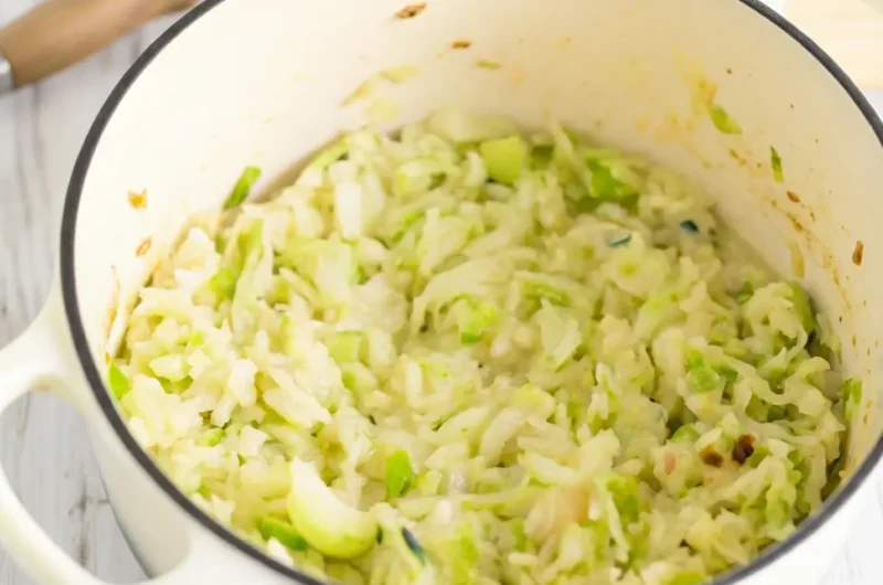 A beautiful 4:3 hero shot of the finished Irish Potatoes And Cabbage, with its creamy, light green and off-white texture, served in a white enameled cast iron pot with a black rim. Bathed in natural morning light on a marble countertop, with a subtle wooden accent in the background. Fresh herbs in a minimalist ceramic bowl are softly blurred, a pristine wooden cutting board partially visible. Soft shadows, warm tones, clean and tidy presentation.