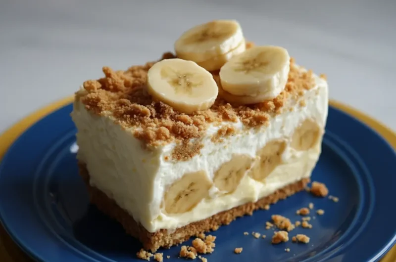 A perfect slice of No-Bake Banana Pudding Cheesecake, showcasing its distinct layers of golden graham cracker crust, creamy white filling with visible banana slices, and a generous topping of whipped cream, more banana slices, and crumbled graham cracker crumbs. The dessert is on a minimalist white plate on a marble countertop with natural morning light creating soft shadows and warm tones. A wooden cutting board and fresh herbs are subtly blurred in the background, creating a clean and tidy presentation. (4:3 ratio)