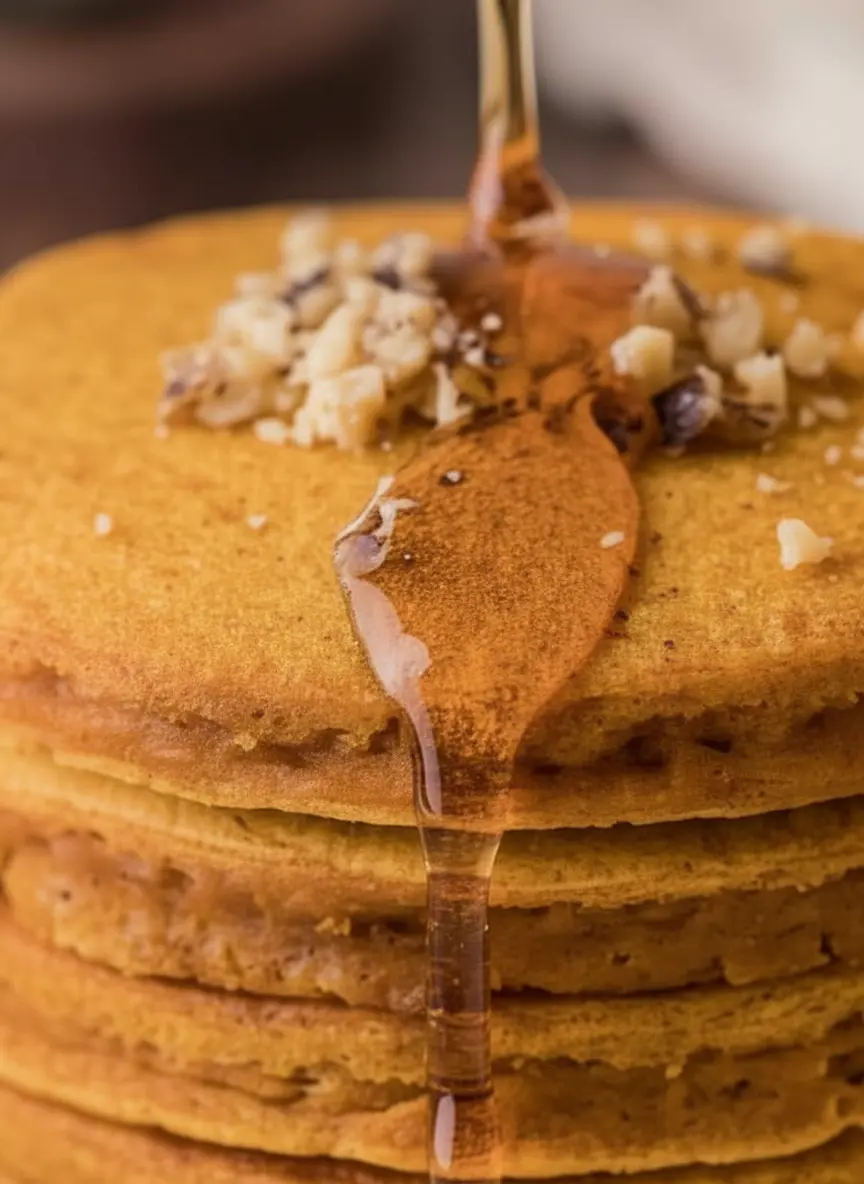 An overhead shot of bowls filled with fresh ingredients for pumpkin pancakes: a bowl of vibrant orange pumpkin puree, another with dry ingredients (flour, spices), and a whisked wet mixture in a third. The ingredients are neatly arranged on a marble countertop with a wooden cutting board in the background, bathed in natural morning light from an east window. Soft shadows. (3:4 ratio)